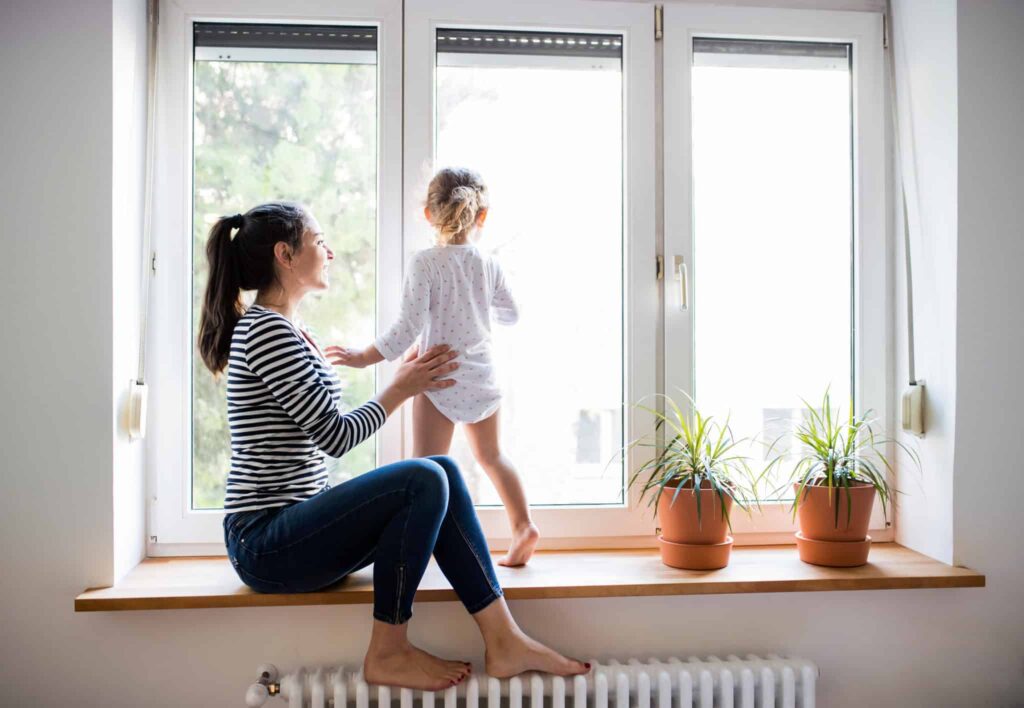 A woman and her child enjoy a peaceful moment by the window, surrounded by thriving potted plants—a reflection of the comfort and trust Bell Brothers brings to homes across Northern California. With our No Surprise Guarantee, thoroughly background-checked technicians, and upfront pricing, families just like yours count on our reputable service for total peace of mind.