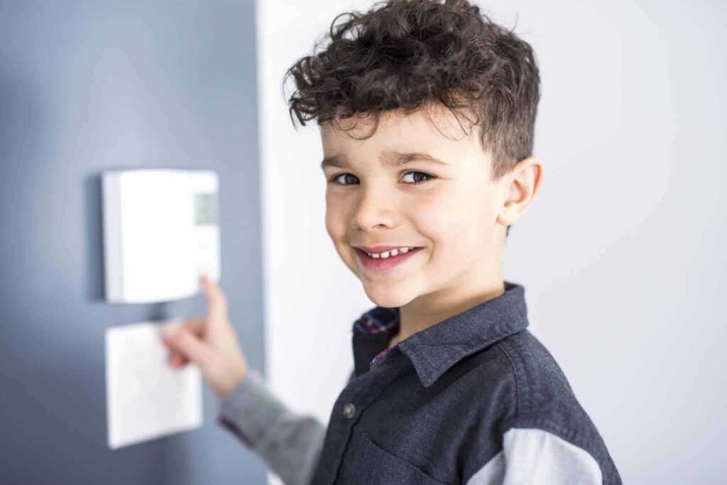 A smiling young boy adjusts a wall-mounted thermostat, highlighting the comfort and peace of mind Bell Brothers delivers to Northern California families. With background-checked technicians, upfront pricing, and our trusted No Surprise Guarantee, we’re proud to be the reliable choice for home services in your community.