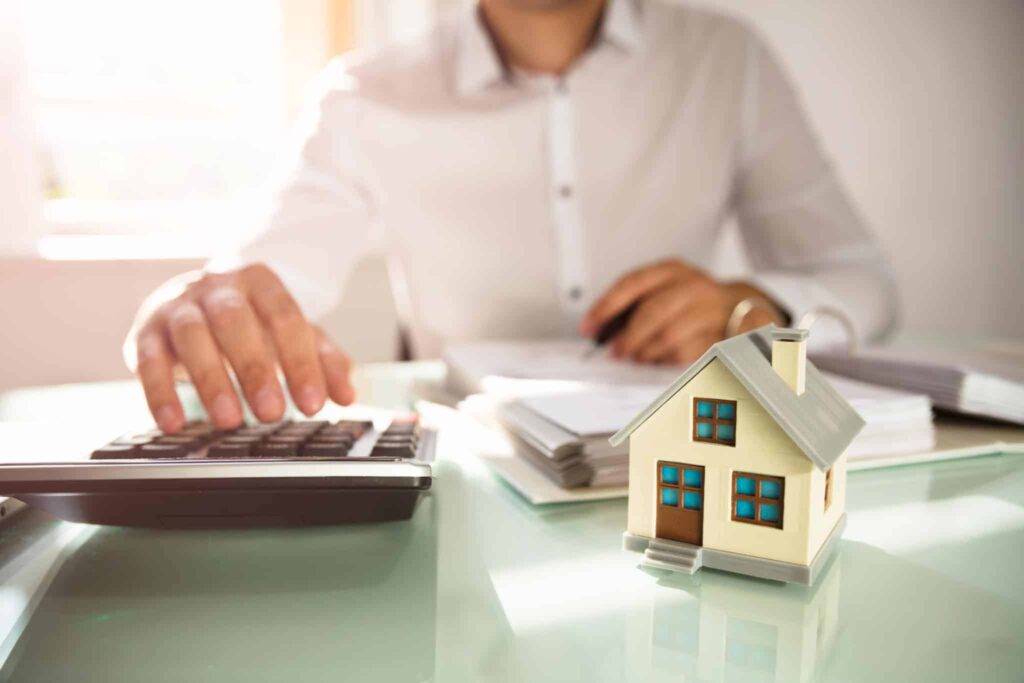 A trusted Bell Brothers technician, fully background-checked, reviews upfront pricing details with a homeowner, using a calculator at a desk with paperwork and a miniature house. This image highlights Bell Brothers’ No Surprise Guarantee and their strong reputation for honest service throughout Northern California communities.