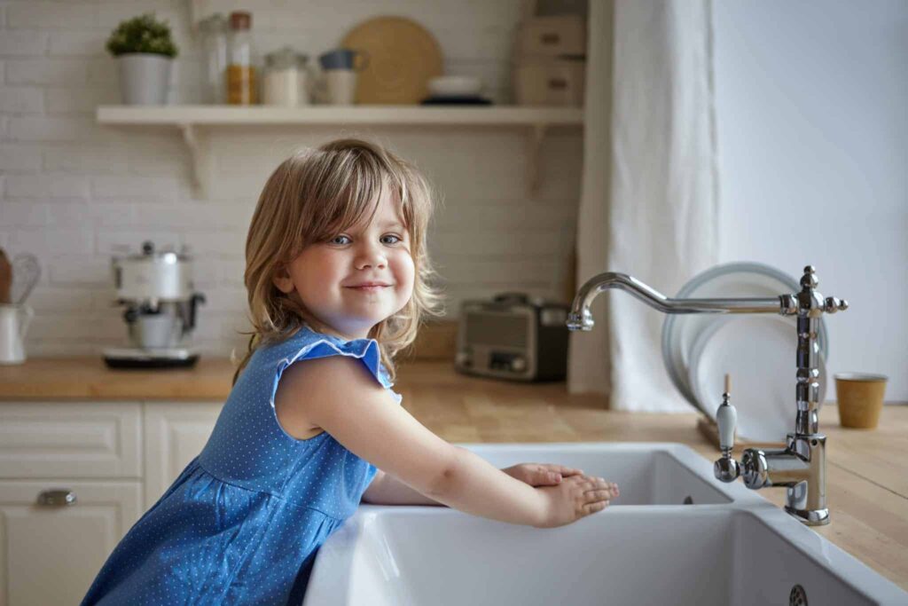 A young girl in a blue dress smiles at the camera while washing her hands at a kitchen sink with white walls and wooden countertops. At Bell Brothers, families across Northern California trust us to keep their homes comfortable, thanks to our No Surprise Guarantee, background-checked technicians, and honest upfront pricing. Our strong reputation is built on service you can count on—every time.