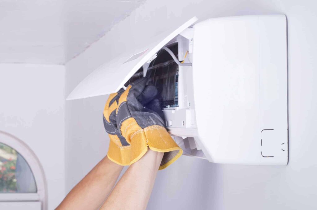 A Bell Brothers technician, wearing protective gloves, carefully opens the front panel of a wall-mounted air conditioning unit for professional maintenance. With our No Surprise Guarantee, thorough background-checked professionals, and clear upfront pricing, you can trust Bell Brothers’ strong reputation for reliable service throughout Northern California communities.