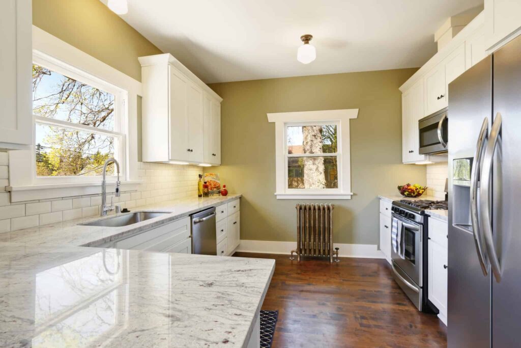 A beautifully updated kitchen featuring white cabinets, stainless steel appliances, marble countertops, light green walls, and a hardwood floor with plenty of natural light. At Bell Brothers, our carefully background-checked technicians deliver trusted service to homes like yours across Northern California. Enjoy peace of mind in your kitchen thanks to our No Surprise Guarantee and upfront pricing—just some of the reasons local communities count on Bell Brothers for all their home comfort needs.