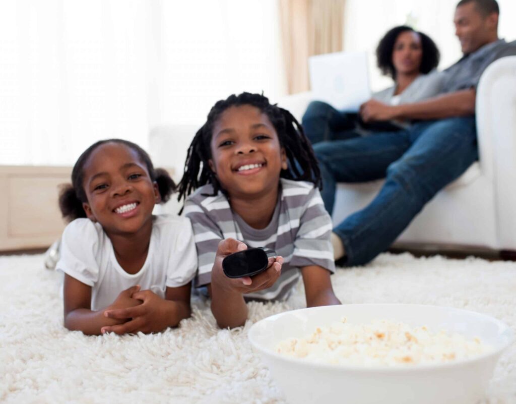 A happy family enjoys a cozy moment together at home—a pair of children relax on the carpet with popcorn and a remote, while two adults unwind on the couch behind them. Thanks to Bell Brothers’ trusted heating and cooling service, families across Northern California experience comfort and peace of mind. With our No Surprise Guarantee, background-checked technicians, and transparent upfront pricing, you can count on reliable service from a team with an outstanding local reputation.