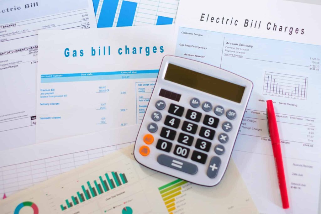A calculator and red pen rest on top of detailed gas and electric bills, surrounded by charts and graphs reviewing utility costs—reflecting Bell Brothers’ commitment to transparency, with upfront pricing, background-checked technicians, and our trusted No Surprise Guarantee proudly serving communities throughout Northern California.