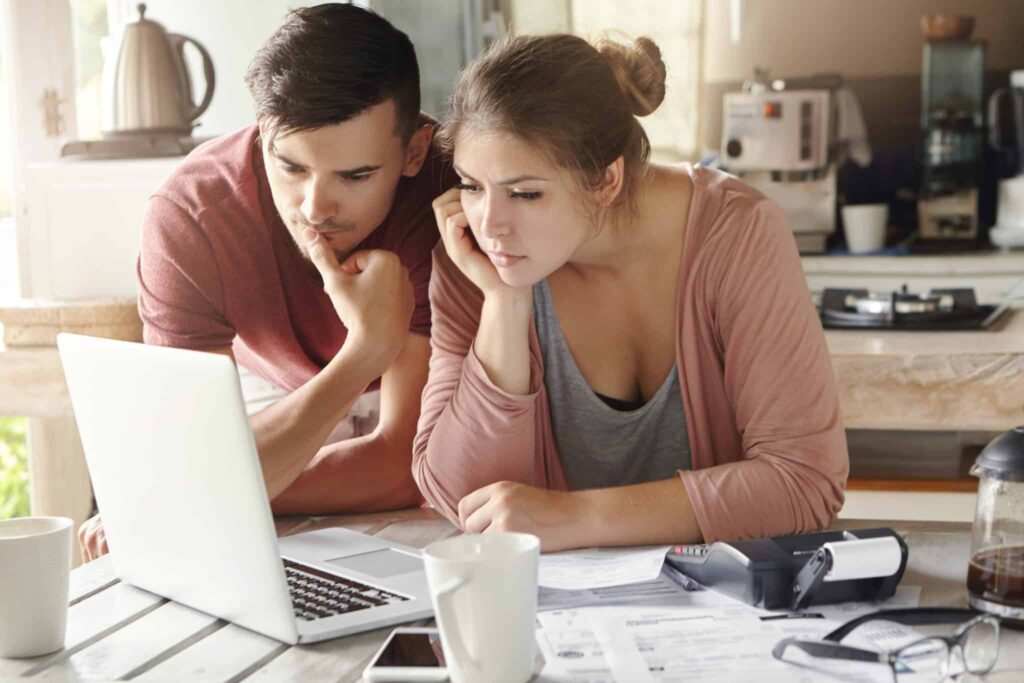 A man and woman sit together at their kitchen table, reviewing information on a laptop with paperwork, a calculator, and coffee mugs nearby. They look confident and at ease, knowing they can count on Bell Brothers’ trusted service—including background-checked technicians, transparent upfront pricing, and the No Surprise Guarantee that has earned Bell Brothers a strong reputation in Northern California communities.