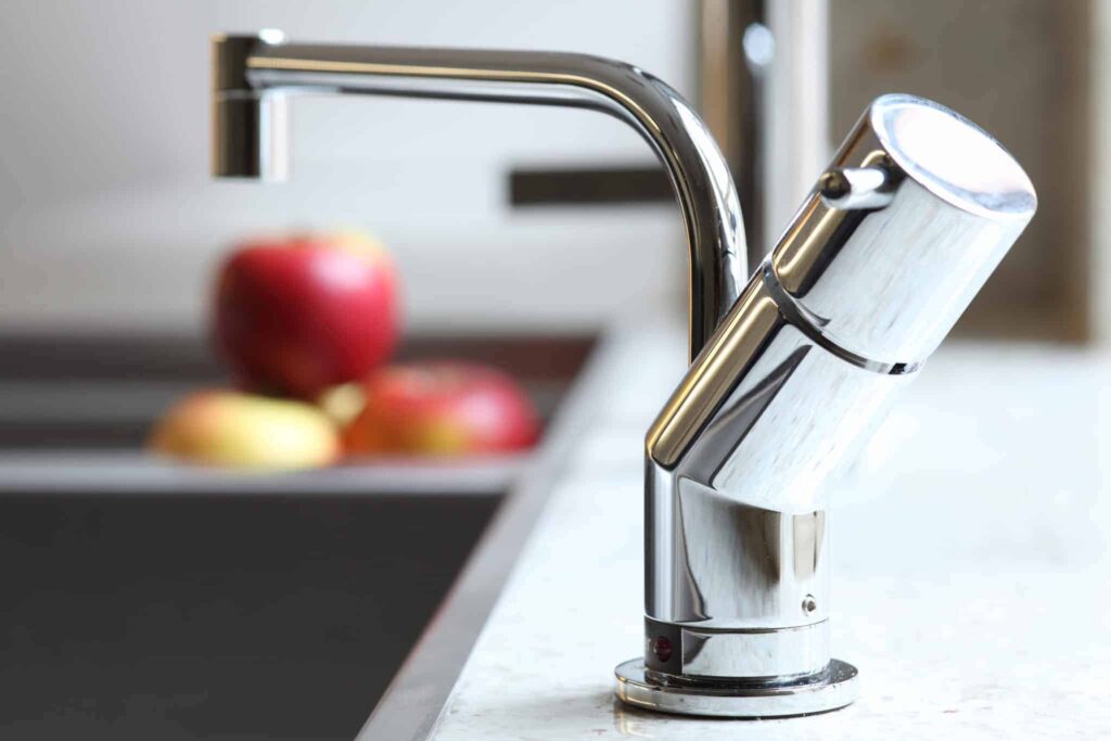 Close-up of a modern chrome kitchen faucet expertly installed on a countertop, with fresh apples and a sink softly blurred in the background. At Bell Brothers, our background-checked technicians deliver trusted service with upfront pricing and our No Surprise Guarantee—earning us a strong reputation for quality throughout Northern California communities.