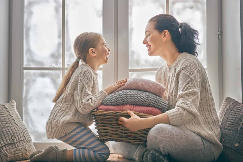 A woman and a young girl share a warm smile by the window, comfortably wrapped in neatly folded knitted blankets. Thanks to Bell Brothers’ trusted service—including our No Surprise Guarantee, background-checked technicians, and honest upfront pricing—families across Northern California can feel confident their homes are in safe hands.