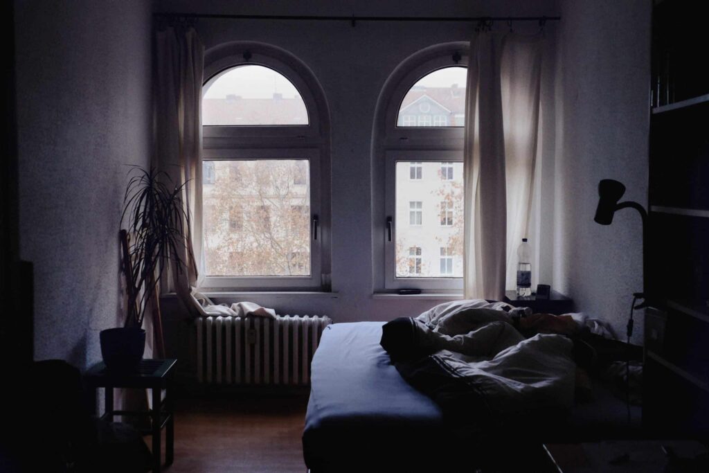 A cozy bedroom with a gently rumpled bed, a cheerful potted plant, and sunlight filtering through two arched windows that frame views of trees and nearby buildings. Trust Bell Brothers—serving Northern California communities with background-checked technicians, upfront pricing, and our No Surprise Guarantee for comfort you can count on.