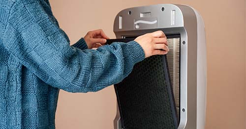 Image: a person changing the filter in their air purifier.