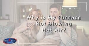 Image: couple bundled up on the couch drinking warm beverages, cover image for Why is My Furnace Not Blowing Hot Air?
