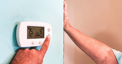 Image: a person adjusting the thermostat on a wall.